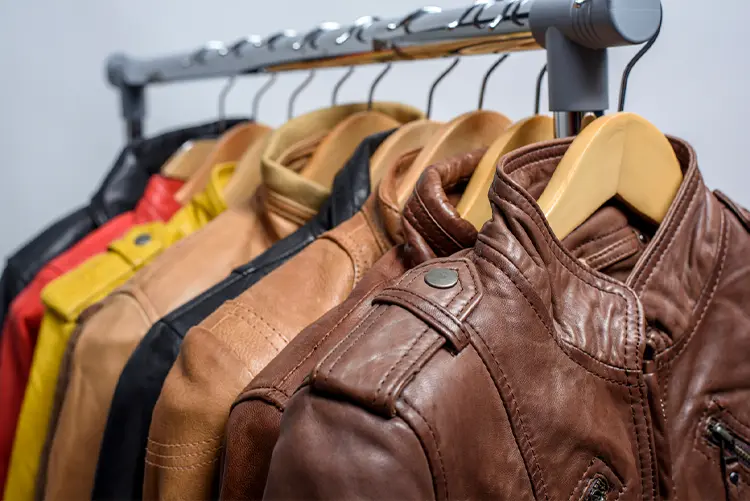 Several leather jackets in various colors hang on wooden hangers on a metal clothing rack.