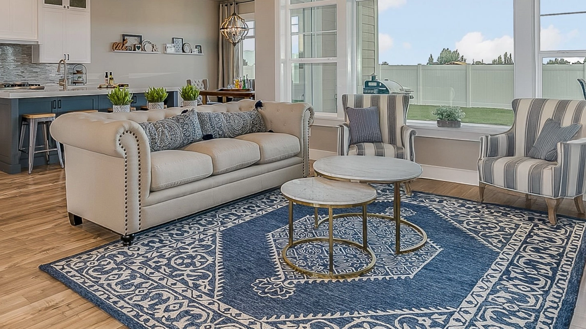 A modern living room with a beige sofa, two striped armchairs, nested round coffee tables, and a blue patterned rug on wooden floors.